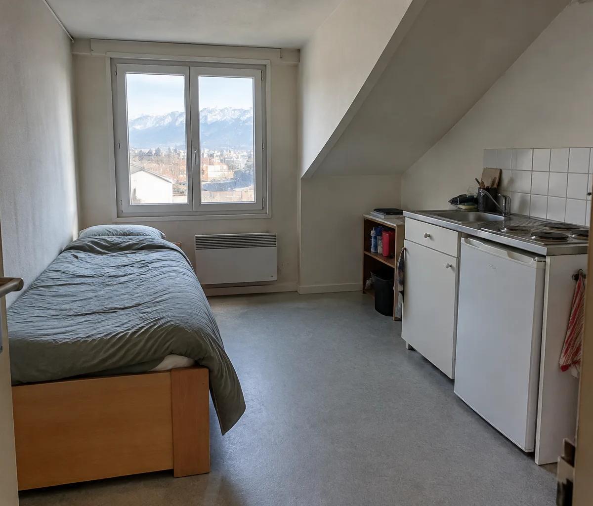 Studio d'une quinzaine de mètres carrés : lit, kitchenette et convecteur électrique sous la fenêtre